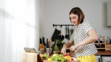 Kafkasyalı anne, modern mutfakta dizüstü bilgisayarda yemek tarifine bakarken salata yapmak için yemek hazırlıyor. Yetenekli ev bekçisi taze sebze kullanarak kahvaltı hazırlıyor. Pedagoji.