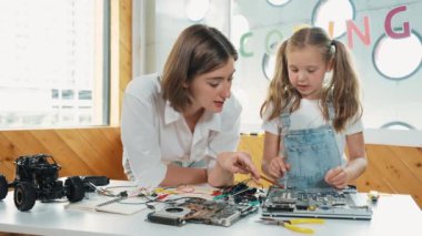 Genç, zeki, beyaz bir öğretmen öğrencilere elektronik kurulun bir parçasını öğretiyor. Uzman kız dijital elektrikli aletleri öğreniyor ve cips ve kablolarla ana kartı tamir ediyor. Etkinlik.