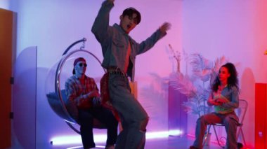 Çok kültürlü bir arkadaş kürsüde otururken Asyalı yetenekli bir dansçı modern müziğe geçiyor. Profesyonel dansçı, hipster takımı tezahürat yaparken ve desteklerken enerjik adımlar atıyor. Mutluluk.