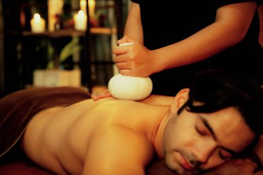 Sıcak bitkisel top spa masaj vücut tedavisi, masör erkek vücuduna nazikçe şifalı bitki torbası bastırıyor. Aromaterapi tesisinin sakinliği ve dinginliği kaplıca salonundaki mumların sıcacık ışığında. Sessiz.