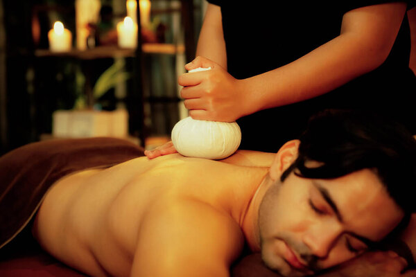 Горячие травяные шарики спа-массаж тела, массажист мягко сжимает травяной мешок на теле человека. Спокойствие и спокойствие ароматерапевтического отдыха при теплом освещении свечей в спа-салоне. Quiescent
