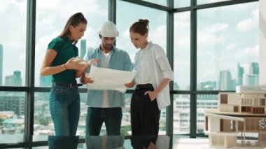 Proje planına bakarken tasarımla ilgili düşünen, paylaşan, beyin fırtınası yapan profesyonel mimar mühendis takımı. Genç bir mimar, genç ve güzel bir menajer not alırken elinde bir plan tutuyor. İzleme