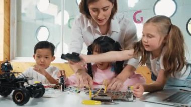 Genç, beyaz bir öğretmen çeşitli öğrencilere elektronik yönetim kurulunu öğretiyor. Çok kültürlü çocuklar dijital elektrikli aletleri ve ana kartı çip ve kablolar kullanarak tamir etmeyi öğrenirler. Etkinlik.