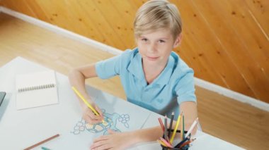 Yaratıcı resim boyayan ve sanat dersinde okuyan mutlu çocuk. Sevimli beyaz çocuk çevrimiçi test yaratıcı öğrenme eğitiminde renklendirme kitabı öğrenmekten zevk alıyor ya da heyecan duyuyor. Üst Manzara. Etkinlik.