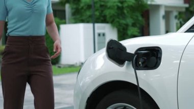 Bir kadın evinde elektrikli araç şarj aletinin fişini çekiyor. İlerici bir yaşam tarzında elektrikli araçların kullanımı, temiz ve sağlıklı bir çevreye katkıda bulunur..