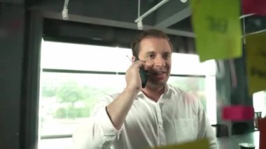 Profesyonel işadamı renkli yapışkan notlara yazılmış pazarlama stratejisi fikrine bakarken müşterilerine telefon ediyor. Proje yöneticisi duvardaki telefon analiz verileriyle konuşuyor. Yönlendirici.