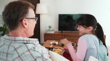 Grandfather and granddaughter eat french fries watch interesting entertainment on TV. Senior use technology communicate with young generation cross generation gap strengthen family bond. Divergence.
