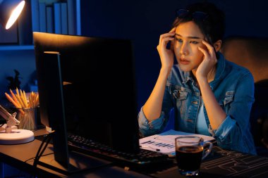 Stresli, genç, güzel Asyalı yaratıcı proje yaratıcısı sosyal medyayı araştırmak için bilgisayara bakıyor ve geceleri daha çok neon modern ofisin planlama kanalı stratejisine ulaşılıyor. Taktik.