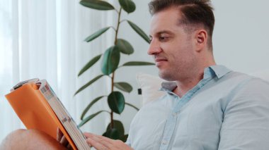 Orta yaşlı bir adam elinde kahve fincanıyla kanepede oturup ders kitabı okuyarak sosyal ve teknolojik meslekler hakkında bilgi artışı yapar ya da çocukları iyi bir yetişkin olarak yetiştirir. Hayat boyu öğrenme konsepti. Uyumsuzluk.