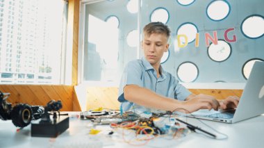 Akıllı mutlu çocuk araba modelini tamir etmek için elektronik alet kullanmayı öğreniyor ya da inceliyor. Lise öğrencisi STEM sınıfında otururken robotik makineleri tamir etmek için elektrikli aletler üzerinde çalışıyor. Öğretim.