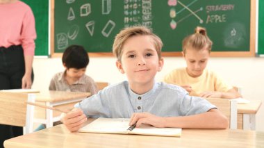 Çekici beyaz çocuk okulda matematik okurken kameraya bakıyor. Çeşitli şirin öğrenciler test yaparken öğretmen Asyalı çocuklara soru sorup tahtaya kağıt doğrultuyor. Pedagoji.