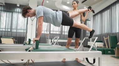 Yetenekli pilates eğitmeni, yenilikçi bir makinede bacak uzantısı olan bir tahtada müşteriye yardımcı olur. Bayan antrenör dengeyi geliştirmek için kalas değişimine yardımcı oluyor. Alışkanlık.