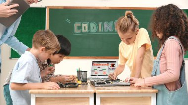 Öğretmenler tableti tutarken ve BTMM teknoloji sınıfında çevrimiçi yazılımı açıklarken ana ekranda dizüstü bilgisayar mühendisliği komut yazısıyla birlikte çalışan çeşitli öğrenci grubu. Pedagoji.