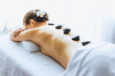 Lüks tatil köyündeki kaplıcalarda sıcak taş masajı. Gün ışığı sükunet ortamında, mutlu kadın müşteri bazalt taş masajından zevk alıyor. Rahatlatıcı bir sıcaklıkla vücudun üzerinde süzülüyor. Sessiz.