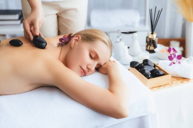 Lüks tatil köyündeki kaplıcalarda sıcak taş masajı. Gün ışığı sükunet ortamında, mutlu kadın müşteri bazalt taş masajından zevk alıyor. Rahatlatıcı bir sıcaklıkla vücudun üzerinde süzülüyor. Sessiz.