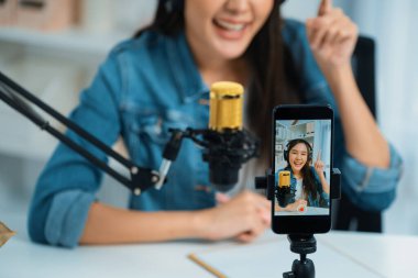 Asyalı sunucu canlı yayında canlı yayında canlı yayında sosyal medyada kulaklık takarak konuşuyor. Dinleyicileri modern stüdyoda koçluk yaparak selamlıyor. Taktik.