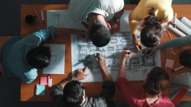 İnşaat mühendisi ekibinin renkli paletlerle toplantı masasında yazı yazması. Yönetici proje planlarına bakarken bir grup farklı insan plan yapıyor ve not alıyor. Sempozyum.