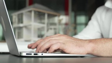 Kabiliyetli beyaz mimar el yapımı ev tasarımını dizüstü bilgisayardaki model ve plan ile karşılaştırın. Laptop analiz verilerini kullanan profesyonel proje yöneticisi. Eline odaklan. Yönlendirici.