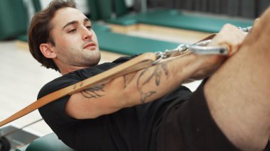 Adam pilates reformatörünü kullanarak çekirdek güçlendirme egzersizi yapıyor. Kolunu ve omzunu güçlendirmek için yüzlerce pozla reformcu üzerinde poz verirken mutlu antrenör pilatesi yakın çekim. Alışkanlık.