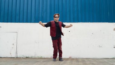 Beyaz arka planda break dans pratiği yapan yakışıklı bir sokak dansçısı. Hip hop tarzı giyinen sporcu, mavi arka planlı bir sokakta müzik eşliğinde ayak sesleri çıkarıyor. Açık hava sporu 2024 hiphop..