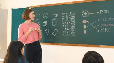 Tebeşir alırken ve ilkokulda teoriyi açıklarken sınıfta matematik sorusunu cevaplamak için karatahta yazan beyaz öğrenci. Çeşitli çocuklar matematik dersinde öğreniyor ve çalışıyor. Pedagoji.