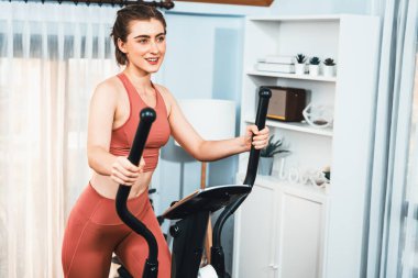 Spor ve atletik bir kadın, evdeki fiziğe ve sağlıklı spor yaşam tarzına uygun vücut egzersizi sırasında eliptik koşu makinesiyle koşuyor. Gaiety evde egzersiz eğitimi.