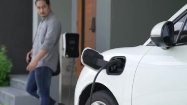 Adamın biri evinde elektrikli araç şarj aletinin fişini çekiyor. İlerici bir yaşam tarzında elektrikli araçların kullanımı, temiz ve sağlıklı bir çevreye katkıda bulunur..