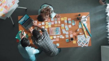 Gündelik kıyafet giyen, dizüstü bilgisayara bakan ve fikir paylaşan iş ekibinin zaman atlaması. Yapışkan notlar ve kulaklıkla masada çalışan ve renk paletini kontrol eden yöneticinin hava görüntüsü. Sempozyum.