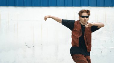 Beyaz arka planda break dans pratiği yapan yakışıklı bir sokak dansçısı. Hip hop tarzı giyinen sporcu, mavi arka planlı bir sokakta müzik eşliğinde ayak sesleri çıkarıyor. Açık hava sporu 2024 hiphop..
