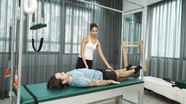 Cadillac ekipmanları üzerinde bacak kaldırma egzersizinde müşteriye yardımcı olan yetenekli pilates eğitmeni. Kadın antrenör, Cadillac 'ın bacak gerdirme hareketine yardım ediyor. Temel bağlantıyı geliştirmek için, bacak esnekliği için. Alışkanlık.