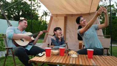 Aile birlikte kamp yapıyor. Baba gitar çalar, anne kız selfie çeker. Ebeveynler, genç nesil arasında iletişim kurmak ve zaman geçirmek için açık hava kamp faaliyetlerini kullanırlar. Uyumsuzluk.