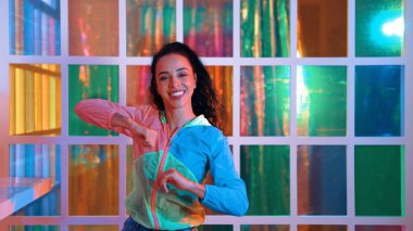 Neşeli İspanyol kız gece kulübünde renkli giysiler giyerken neon ışıkta müzik eşliğinde hareket ediyor. Sokak dansçısı kameraya bakarken hareketli adımlar atıyor. Mutluluk.