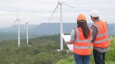 Erkek ve kadın mühendisler kırsal kesimdeki bir tepenin tepesinde ya da dağda rüzgar çiftliğinde çalışıyorlar. Yenilenebilir ve sürdürülebilir enerjinin gelecekteki üretimi için yenilikçi idealler.