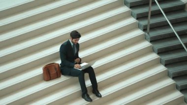 Merdivenlerde dizüstü bilgisayar kullanarak yatırımcıların çalışma ya da planlama stratejisinin en üst görüntüsü. Modern bir otelde dizüstü bilgisayar kullanarak veri analizi yapan takım elbiseli profesyonel bir iş adamı. Sevinçli..