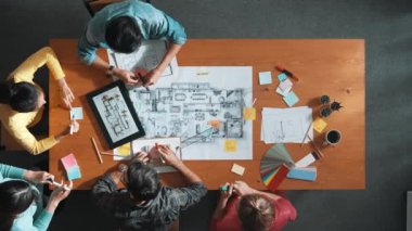 Toplantı odasındaki planlara bakan akıllı mühendisin yukarıdan görünüşü. Yetenekli mimar takımı konuşur ve tartışır. Proje planında planlarla toplantı masasını incelerken. Sempozyum.