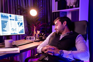 Akıllı iş adamı çalışma masalı sandalyeye yaslanıyor, bitmemiş ürün satış kanalı raporu, uzun zamandır güncellenmiş pazar verilerini bekliyor mor neon ışıklı odada gece geç saatlerde. Tahmin et..