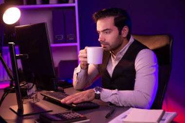 Gülümseyen zeki işadamı, elinde kahve fincanı olan satış ekibiyle buluşuyor ve geceleri Mor Neon Light Home Office 'deki bilgisayar ekranında ürün hedef pazarını araştırıyor. Tahmin et..