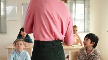 Sınıfta sınıf çalışmalarını anlatırken, sınıfta dolaşan beyaz bir öğretmen. Çekim eğitmeni konuşuyor ve çeşitli öğrenciler çalışırken ya da not alırken dersini anlatıyor. Eğitim. Pedagoji.
