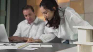 Bir grup mimar mühendis birlikte çalışıyor ve ofis tasarımı hakkında tartışıyorlar. Genç mühendis ev modelini ölçerken yönetici dizüstü bilgisayar kullanıyor. İş tasarımı konsepti. Yönlendirici.