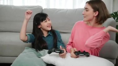 Sevimli anne ve enerjik kız oyun oynuyor ve başarıyı kutlamak için beşlik çakıyor. İşbirlikçi anne, elinde joystick tutarken çocuğunun yanında oturuyor ve kızıyla oyun oynamaya odaklanıyor. Pedagoji.
