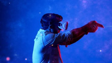 Yetenekli oyuncular silah olarak el ele tutuşup VR gözlük takıp atış oyunu oynayarak metaevrene girebiliyor. Çekici erkek model mavi arka planda dururken hareket ediyor ve oyuncuyu hedef alıyor. Aygıt.