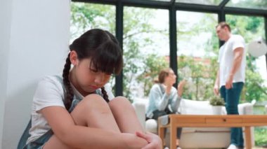Stresli ve mutsuz genç kız köşeye kıvrılıp kulaklarını kapatarak arka planda ebeveyninin tartışmasını engelliyor. Evde aile içi şiddet ve travmatik çocukluk depresyona dönüşür. Titiz