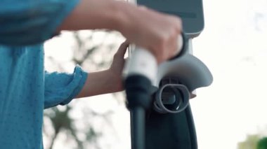 Kapalı alan kadını, doğal yeşil parktaki otoparkta EV elektrikli araba aküsünü şarj ediyor. Sürdürülebilir ve çevre dostu seyahat için şarj edilebilir araç için temiz enerji teknolojisi. Titiz