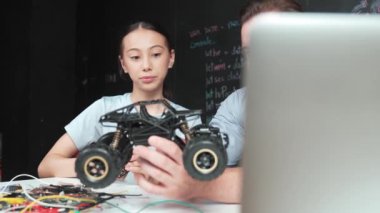 Akıllı öğretmen araba modelini farklı öğrencilere denetliyor. Melez ırk dinleyen liseli çocuklar masada dizüstü bilgisayarı ve kabloları olan robot model sistemini açıklıyor. Öğretim