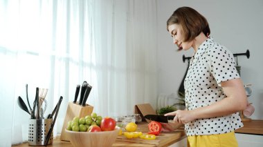 Enerjik anne, mutfak malzemeleri ile çevrili sebzeleri doğrarken modern mutfakta kahvaltı için salata yapıyor. Akıllı kadın temizlikçi yemek pişirir ve yemek hazırlar. Sağlıklı bir yaşam tarzı. Pedagoji.
