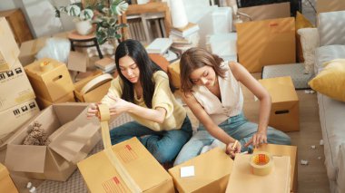 Çekici bir oda arkadaşı oturma odasında paket paketlerken pakette konum yazıyor. Mutlu satıcı birlikte çalışıyor ve teslimat paketini hazırlıyor. Girişimci kargo kutusu paketliyor. Myrmidon.