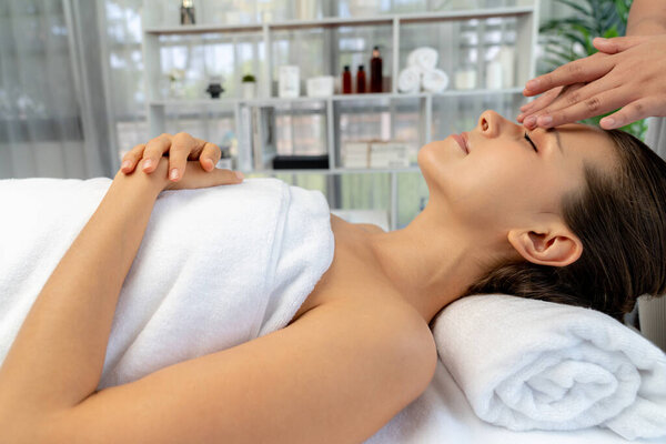 Caucasian woman enjoying relaxing anti-stress head massage and pampering facial beauty skin recreation leisure in dayspa modern light ambient at luxury resort or hotel spa salon. Quiescent
