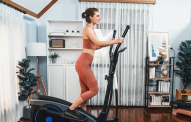 Spor ve atletik bir kadın, evdeki fiziğe ve sağlıklı spor yaşam tarzına uygun vücut egzersizi sırasında eliptik koşu makinesiyle koşuyor. Gaiety evde egzersiz eğitimi.