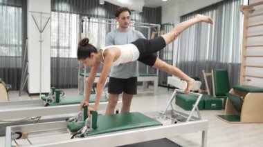 Bir pilates eğitmeni, müşteriye bir ıslah makinesinin tahta varyasyonunda rehberlik eder. Sağlıklı bir kadın, dengeyi geliştirmek için antrenör yardımı ile yenilikçi üzerinde yan kalas değişimi yapıyor. Alışkanlık.