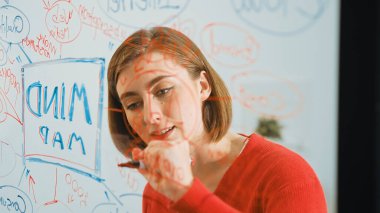 Closeup of young beautiful caucasian business leader presents marketing idea while writing marketing idea on glass board at creative meeting, brain storming discussing, working together. Immaculate. clipart